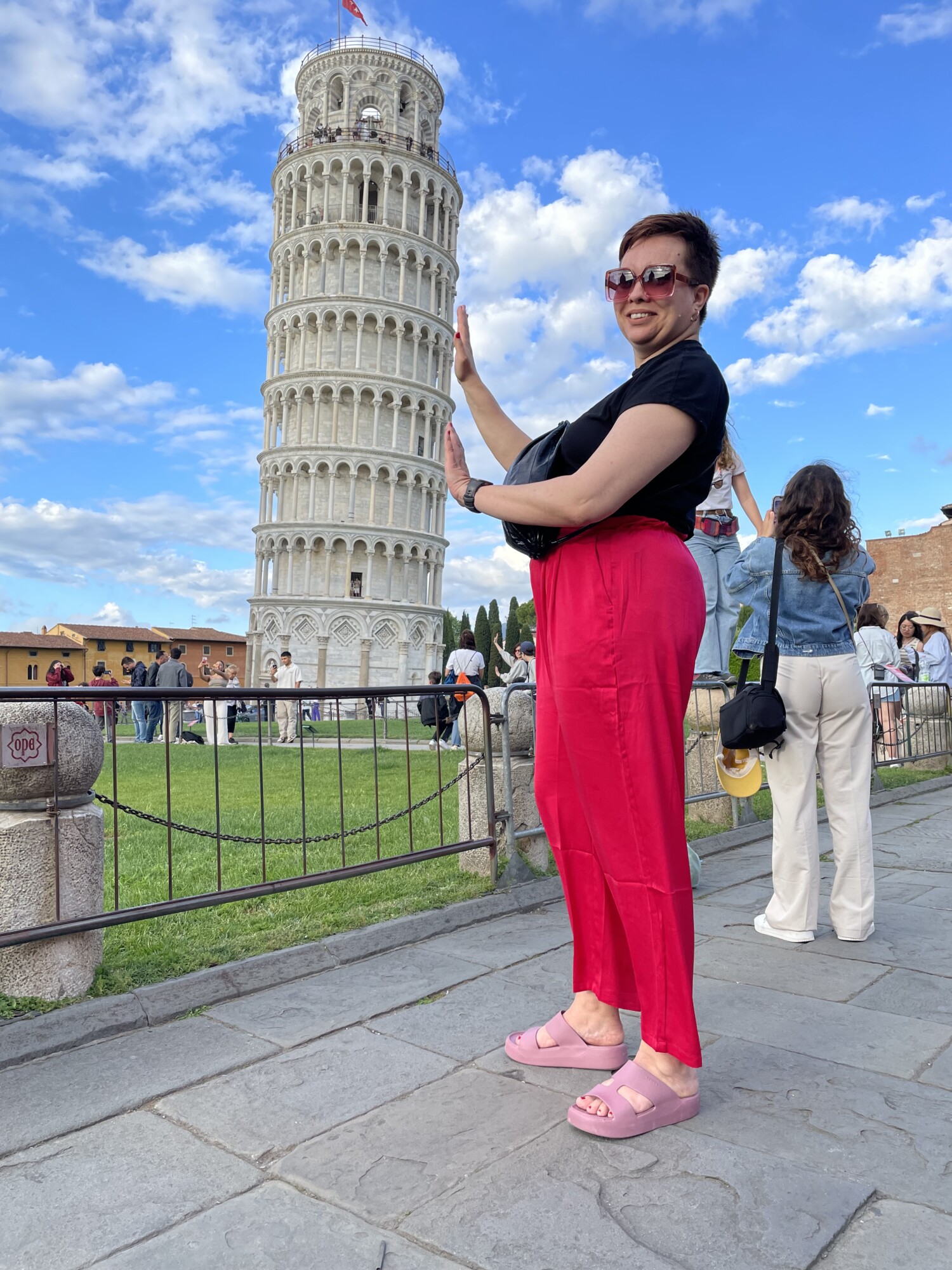 Nainen seisoo Pisan tornin edessä ja näyttää siltä kuin hän pitäisi sitä pystyssä.