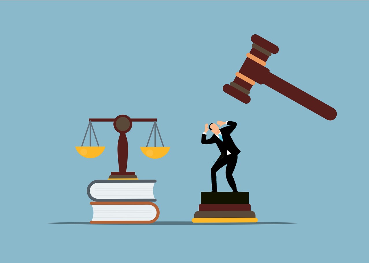 Piirretyssä kuvassa tasolla lakikirjoja ja punnusvaaka, vieressä pieni ihminen joka on jäämässä tuomarin nuijan alle.