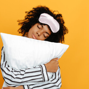 Nuori nainen unimaski otsallaan halaa tyynyä.