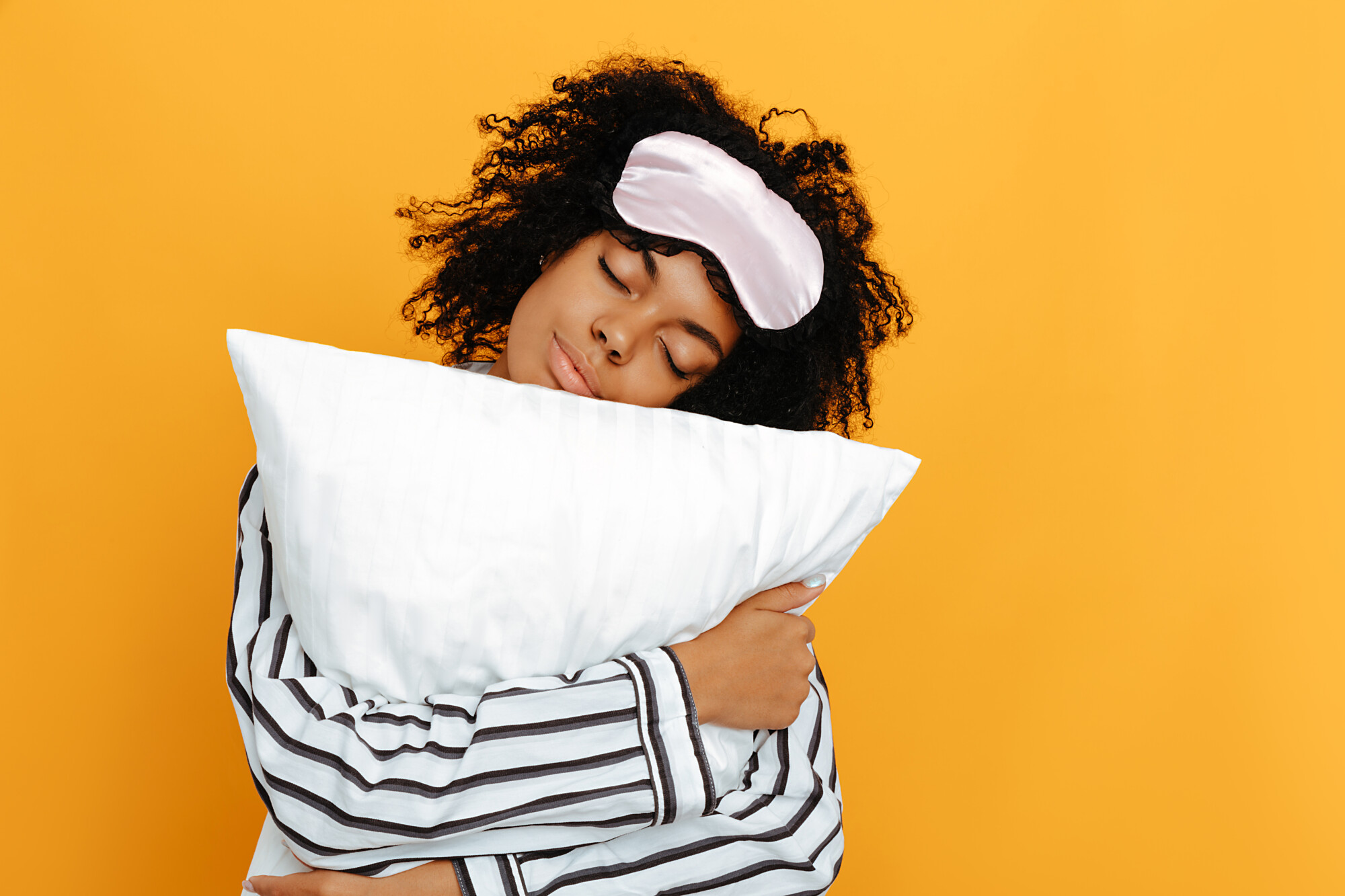 Nuori nainen unimaski otsallaan halaa tyynyä.