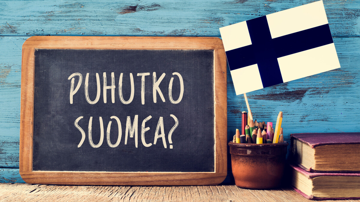 Liitutaululla teksti puhutko suomea? Kynäpurkissa pystyssä suomenlippu