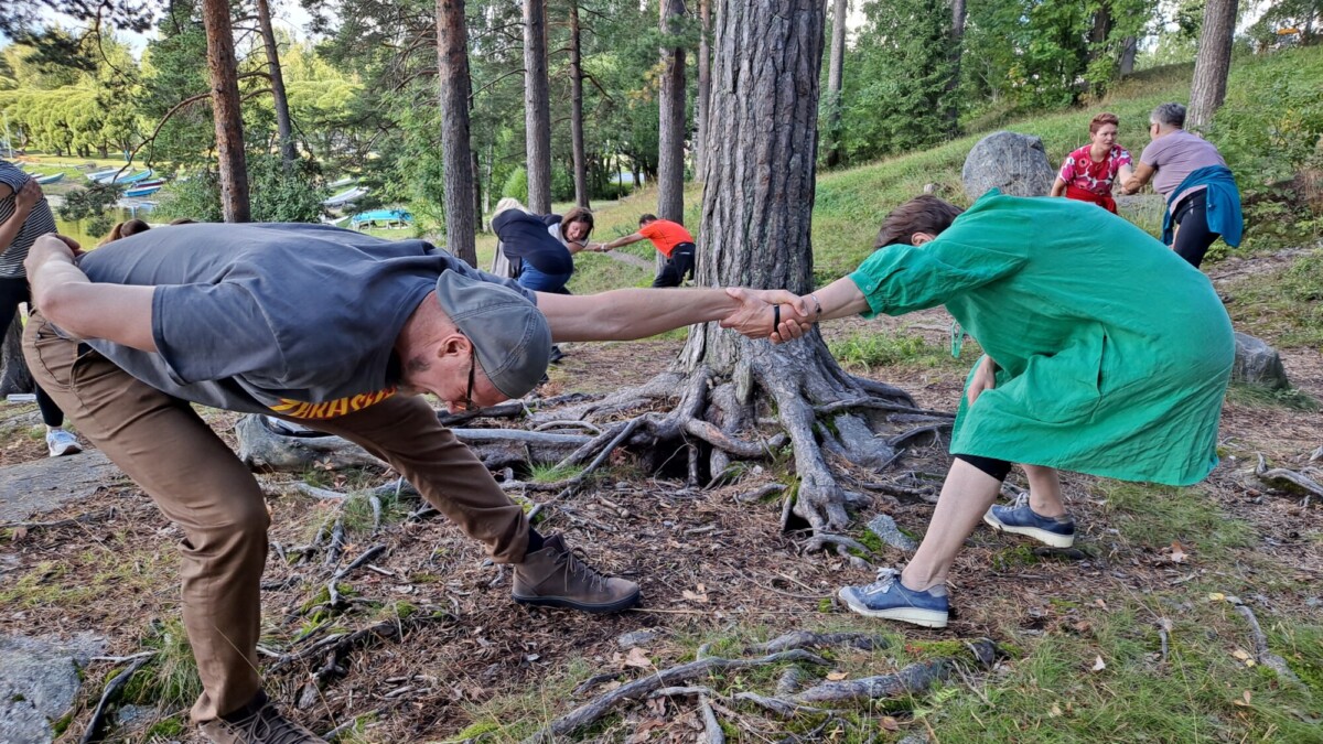 Ihmiset venyttelevät luonnossa puiden ympärillä. 